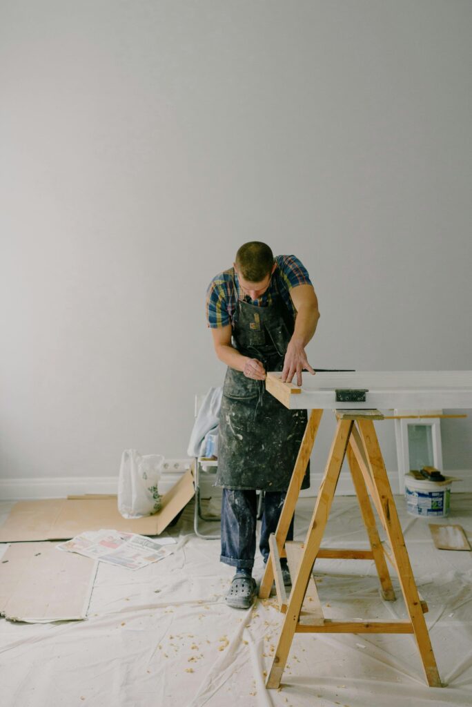 Full length of skilled craftsman in dirty apron repairing and restoration wooden window in light room